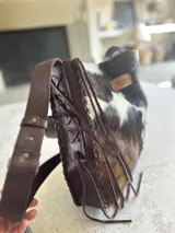 Bolso maxi de cuero con estampado de vaca en blanco y negro, y cuero color chocolate en la parte posterior. Tiene correa larga para colgar al hombro.