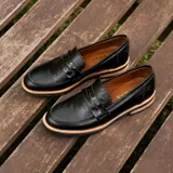 Mocasín de cuero vacuno color marrón, con detalle de antifaz en gamuza. Tiene taco de madera foliado en cuero de 2,5cm y entre suela de goma de 1cm.