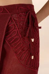 Falda pareo larga color vino, de tejido calado con bordado floral y detalle de cuentas en los pliegues.