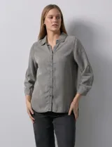Camisa celeste de tencel con cuello con solapa, escote en V, abertura central con botones y mangas 3/4 regulables con presilla y botón.