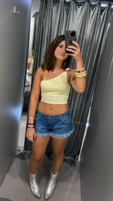 Top amarillo pálido de un solo hombro con detalle de hebilla metálica en el tirante.