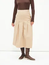 Falda midi color beige con cintura alta y pliegues frontales.