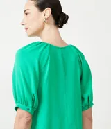 Blusa verde de crepé con cuello redondo, manga corta abullonada y abertura en forma de gota en el escote.