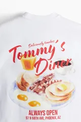 Remera blanca de corte oversized con estampado rojo de la leyenda "Tommy's Diner" en el pecho.