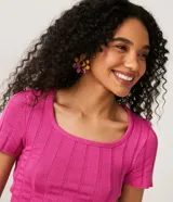 Blusa de punto color fucsia con cuello redondo y mangas cortas. Tiene una malla texturizada con material responsable en la composición.
