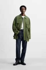 Parka verde militar de tejido técnico ligero, corte relaxed fit, cuello solapa y manga larga. Tiene cuatro bolsillos de plastrón con solapa en el delantero, cintura ajustable en el interior y cierre frontal con cremallera oculta por solapa con botones a presión.