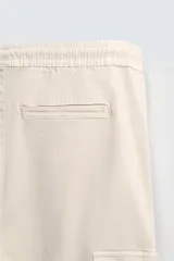 Pantalón cargo negro de corte slim fit, confeccionado en tejido de algodón con cintura elástica ajustable con cordón. Cuenta con bolsillos frontales, traseros y bolsillos tipo parche con solapa en los laterales.