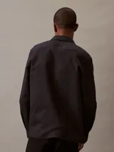 Camisa negra de lino y algodón, de corte clásico, con cuello en punta, cierre frontal con botones y mangas largas con puños abotonados.