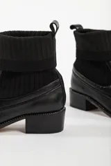 Bota negra con detalle de calcetín, diseño moderno y tacón bajo.