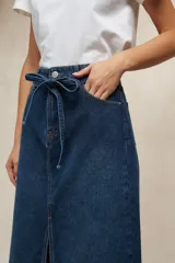 Falda larga de mezclilla color marrón chocolate, de tiro alto con cordón ajustable en la cintura y abertura frontal pronunciada.