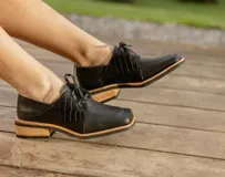 Zapato acordonado de cuero vacuno color marrón oscuro, con suela de goma, horma cuadrada y tacón bajo.