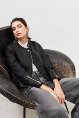 Campera negra de cuero ovino con cierre frontal asimétrico, cuello mao con botón a presión y bolsillos con cierre.