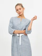 Túnica midi de lino color crudo con finas rayas verticales en tono marrón. Presenta cuello en V con abertura y mangas tres cuartos. La cintura se ajusta con un lazo del mismo tejido, y tiene aberturas laterales en el ruedo.