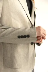 Blazer gris de silueta recta y textura sutil, con solapas de muesca, cierre con dos botones, bolsillos con solapa y puños con cuatro botones.