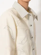 Chaqueta corta color crema de canvas con detalles en cuero genuino en cuello y cartera. Diseño con bordados de hongos y chiles intervenidos con strass.