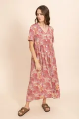 Vestido largo color ladrillo con estampado de hojas en tonos blanco y amarillo. Tiene escote en V, mangas cortas y botones frontales.