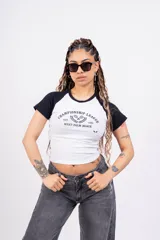 Remera corta blanca con mangas raglán negras, cuello redondo y estampado frontal con el texto "Championship League Est. 1996 West Palm Beach" y dos raquetas de tenis cruzadas.