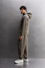 Sudadera con capucha color marrón topo, de corte regular fit, confeccionada en tejido técnico compacto de algodón con elasticidad. Cuenta con cuello subido, manga larga con bolsillo, bolsillos frontales con cierre de cremallera y acabados con rib del mismo tejido.