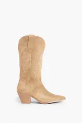 Bota de caña media color beige, confeccionada en suede, con pespuntes decorativos en la caña y la puntera. Presenta un tacón de bloque y punta en pico.