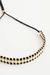 Gargantilla estilo choker con diseño étnico, compuesta por una base de cordón negro entrelazado con piezas cuadradas de vidrio engarzadas en marcos de metal dorado.