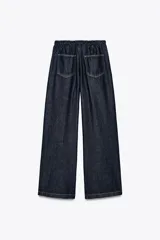 Pantalón de jean azul oscuro, de tiro medio, corte ancho y largo, estilo jogger con cintura elástica ajustable con cordones, bolsillos delanteros de vivo y bolsillos de parche en la espalda.
