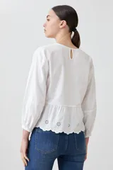 Blusa blanca con calados, cuello redondo, mangas largas abullonadas y corte peplum.