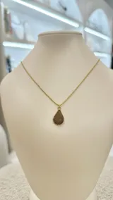 Collar con cadena dorada y dije de amatista en forma de gota con textura brillante.