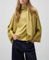 Blusa amplia tipo chal color verde, con cuello drapeado lateral sujeto en hombro con aplique dorado. Mangas rectangulares recogidas en puño.