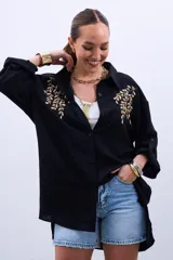 Camisa negra de mangas largas con puños abotonados y bordados dorados en el frente.