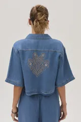 Blusa celeste de denim con cuello camisero, mangas cortas y cierre frontal con botones.