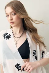 Poncho de gasa liviana color blanco, con bordados florales negros y detalles de borlas en el borde.