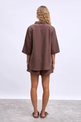 Camisa blanca de manga tres cuartos, con cuello camisero y corte holgado. Presenta un bolsillo de parche en el pecho izquierdo.