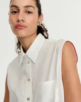 Camisa blanca sin mangas confeccionada en voile de algodón liviano. Tiene cuello camisero, cartera con botones de nácar, bolsillo plaqué en el delantero, costura en centro espalda y recorte en cintura trasera con tajo que se superpone. El ruedo es escalonado, más corto adelante.