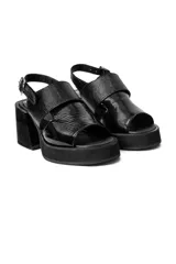 Sandalias negras de charol con plataforma y tacón cuadrado. Presentan tiras anchas cruzadas en el empeine y correa ajustable en el tobillo.