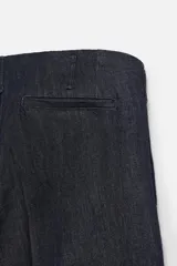 Pantalón de denim azul oscuro, corte wide fit, largo cropped, con pliegues frontales, bolsillos laterales y traseros asimétricos. Cierre frontal con cremallera y gancho metálico oculto.