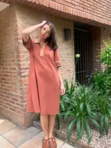 Vestido color ladrillo de tejido de hilo, corte recto, cuello polo con botones y mangas cortas con ribete en color beige.