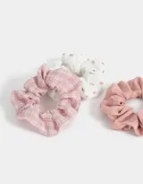Set de tres scrunchies para el pelo con diferentes estampados: uno liso color rosa, uno blanco con estampado de flores pequeñas y uno a cuadros rosa y blanco.