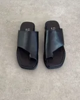 Sandalias negras de cuero vacuno con tira ancha sobre el empeine y espacio para el dedo gordo.