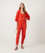 Kimono color naranja de tejido orly con mangas 3/4 con detalle de pompones en el dobladillo, lazo en la cintura y cierre frontal.