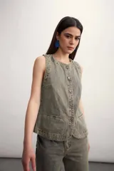 Chaleco de jean color gris con desgaste, sin mangas, con cuello redondo y cierre frontal con botones.