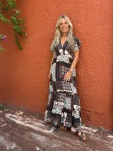 Vestido largo con estampado tipo patchwork en tonos tierra, blanco y azul oscuro. Presenta escote cruzado en V y mangas cortas. La falda es larga y con vuelo.