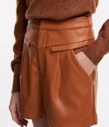 Short corto de cuero sintético color marrón, con cintura alta, bolsillos laterales con solapa y cierre frontal con botón y cremallera.