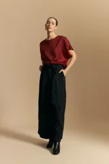 Top negro de manga corta con silueta amplia y caída fluida, confeccionado en un tejido liviano con leve brillo. Presenta un botón de nácar en la espalda con una pequeña abertura y mangas amplias tipo kimono.