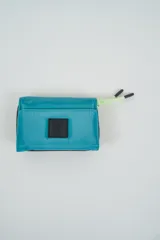 Billetera plegable color turquesa brillante, con cierre de velcro y un parche frontal negro con texto en relieve. Incluye un cordón de ajuste de color verde lima con terminaciones negras.