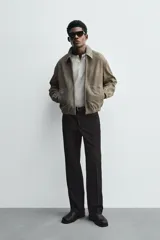 Cazadora de hombre color verde oliva, confeccionada en piel con acabado ante. Presenta un corte boxy fit, cuello solapa, cierre frontal de cremallera, bolsillos delanteros y elásticos en puños y bajo.