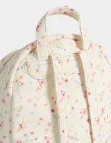 Mochila pequeña de cuerina color crema con estampado de flores pequeñas en tonos rosa, naranja y celeste. Tiene un bolsillo frontal con cierre, correas regulables, manija superior, cierre superior y bolsillos laterales.