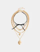 Set de tres collares dorados con diferentes tipos de cadenas y dijes: gargantilla de terciopelo negro con lazo, cadena con dije de corazón y cadena con relicario ovalado con diseño floral.