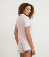 Conjunto de pijama americano compuesto por una blusa de manga corta con cuello solapa y abotonado frontal, y un short con cintura elástica y lazo. El conjunto es liso en color rosa pálido, con vivos contrastantes en el borde de las prendas.