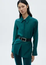Camisa de vestir verde esmeralda de corte recto, con cuello camisero, cierre frontal con botones ocultos y mangas largas con puños abotonados.