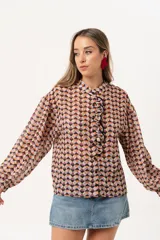 Camisa de gasa estampada traslúcida con diseño geométrico de rombos en tonos lila, naranja y negro. Tiene calce liviano y fluido, abotonado frontal y volado en la cartera.
